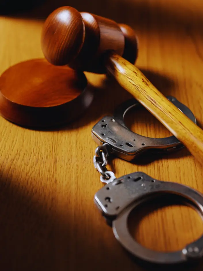 Martelo de juiz (malhete) e um par de algemas de metal sobre uma mesa de madeira.